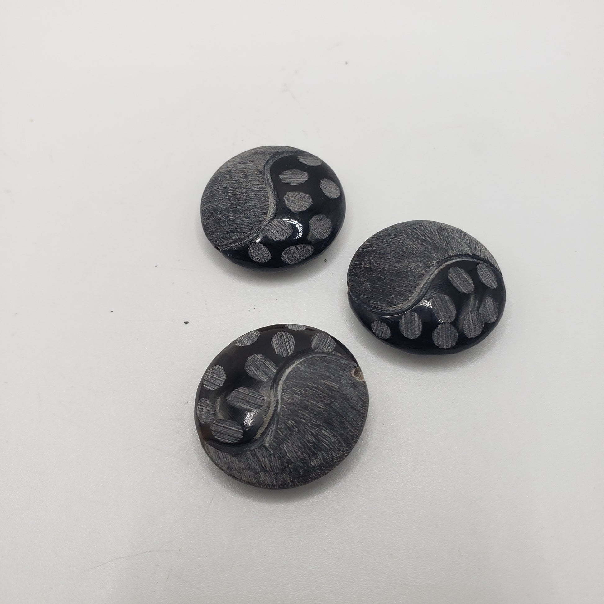 Three Black Yin-Yang Bead Single buttons with a shiny finish, featuring a swirl pattern and small circular indentations. The buttons are placed on a plain white surface.