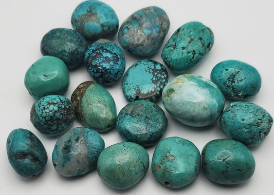 A selection of 20-30mm Turquoise Chunk Singles in an array of blue and green hues, artfully arranged on a white backdrop. The chunks showcase their natural patterns and textures, highlighted by darker speckles and veins.