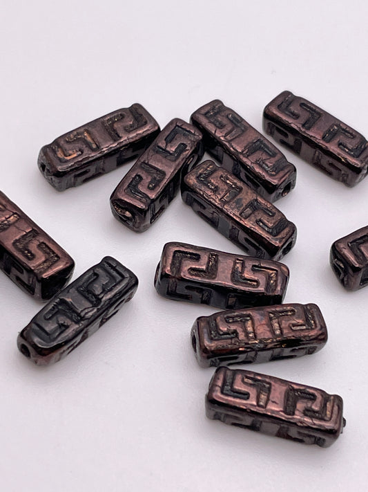 The exquisite 15mm Rectangle Pattern Czech Single Bead showcases a glossy black finish with intricate copper-colored geometric designs set against a pristine white backdrop.