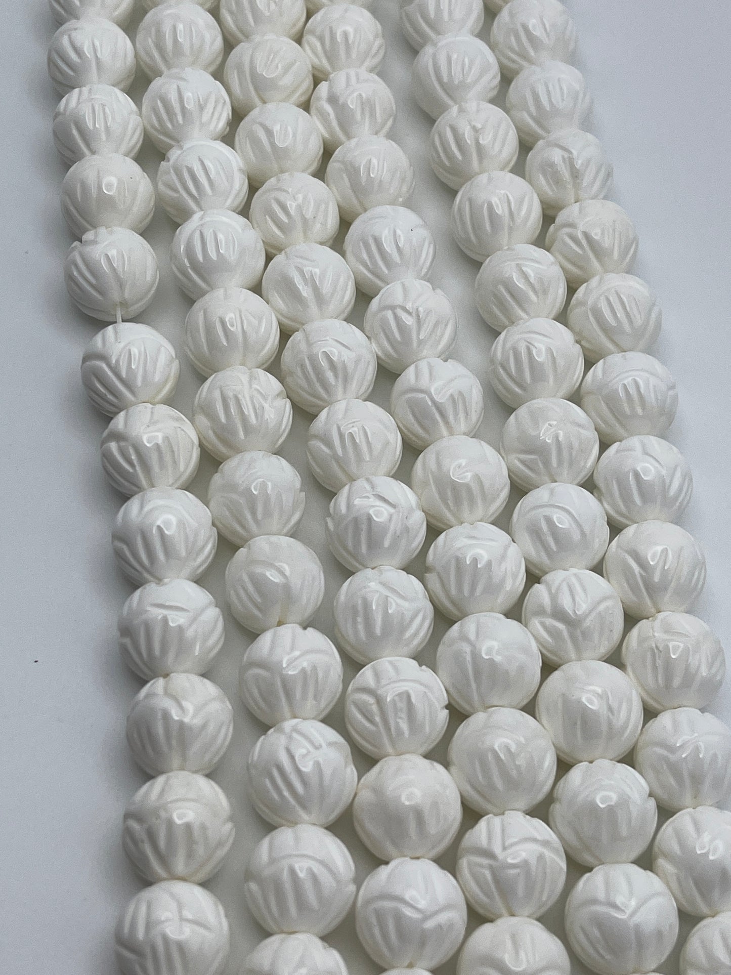 Rows of gleaming, white 12mm Tridacna Shell Carved Singles arranged on a flat surface.